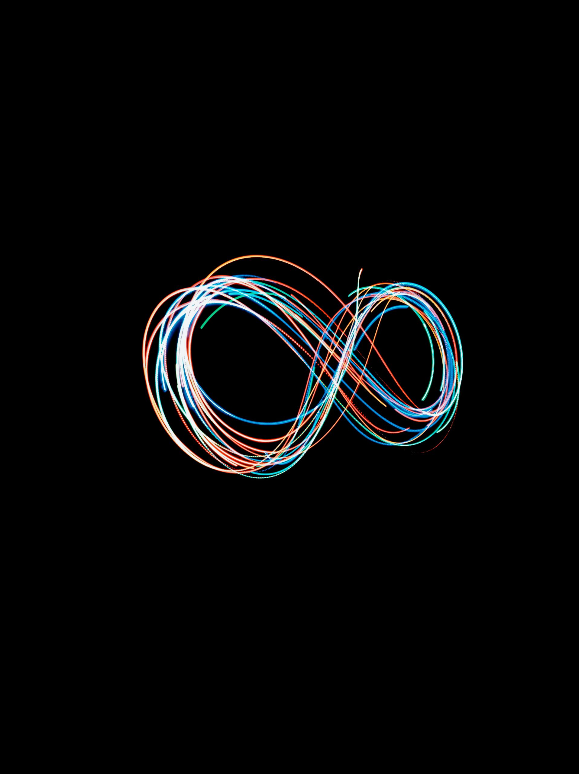 Abstract long exposure shot of colorful light trails forming an infinity symbol against a black backdrop.
